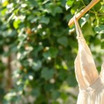 une-robe-dete-elegante-accrochee-a-un-support-en-bois-avec-une-lumiere-naturelle-douce-et-un-fond-de-verdure-luxuriante